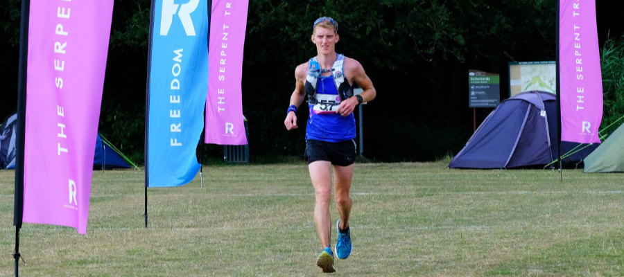 A photograph of a male ultramarathon runner nearing the finish line of a race