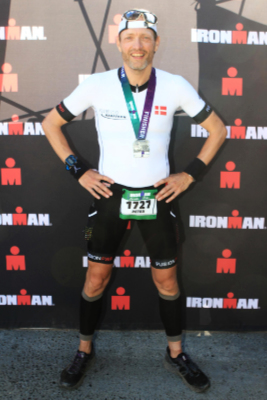 A male triathlete poses in front of Ironman logos