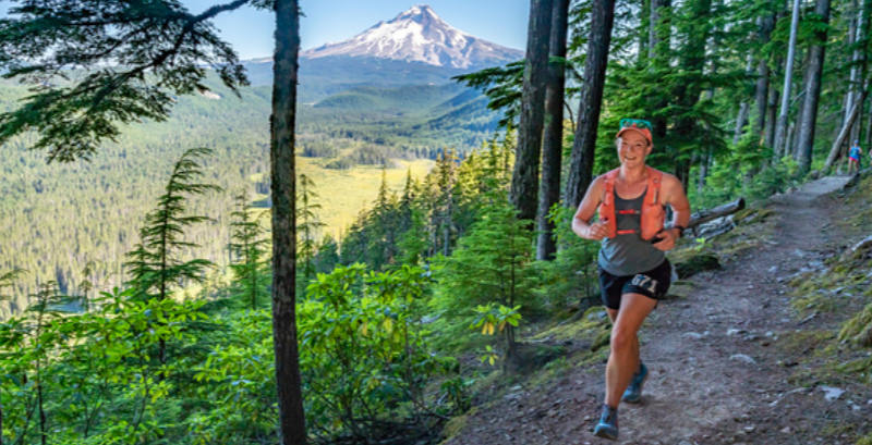 A female ultrarunner runs on a trail with view of Mt. Hood in the distance