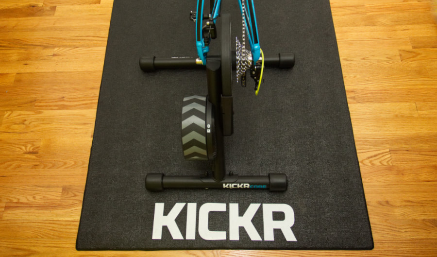 A photograph of a Wahoo KICKR Core with a blue road bike mounted to it on a Wahoo KICKR floor mat on a hardwood floor