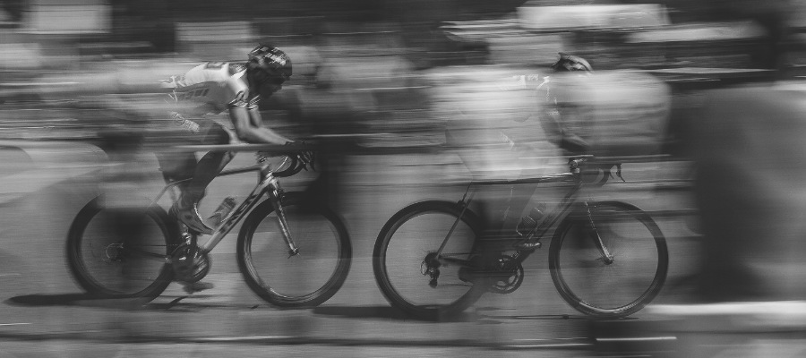 A black-and-white photo of two road cyclists moving quickly on their bikes